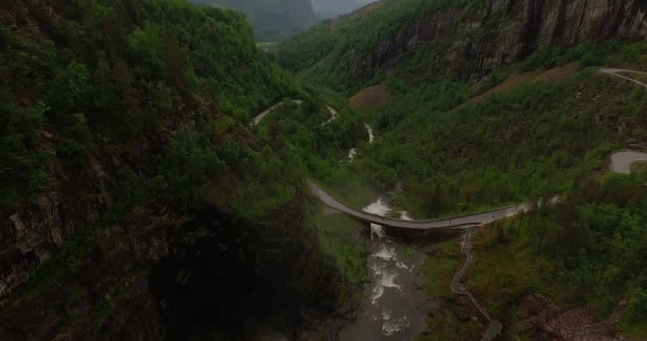 Water flows down a tall cliff towards a bridge