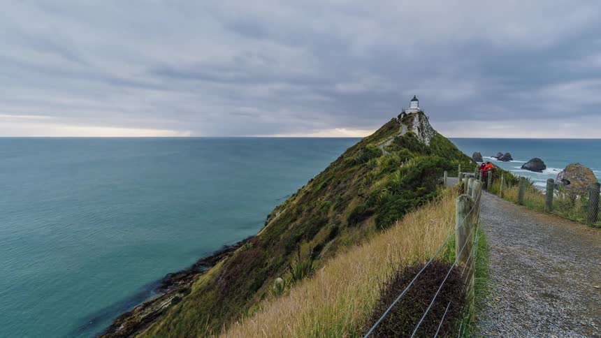 People walk to and from a lighthouse by the water