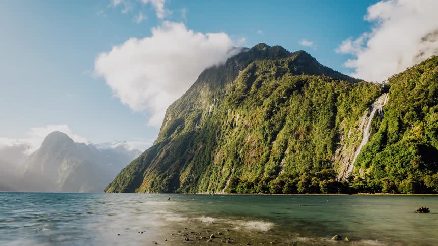 Fluffy clouds leap into the sky around a green mountain