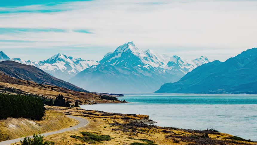 A street curving past a mountainside lake