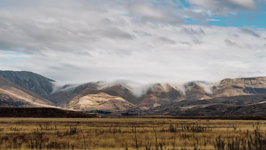 Clouds billow over rocky mountains and flat plains