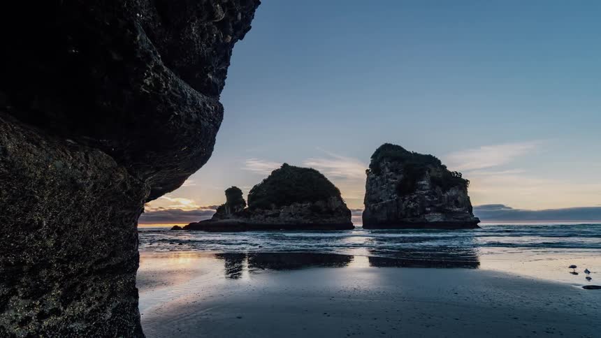 Waves are lapping a beach as a sunny day transitions to dusk
