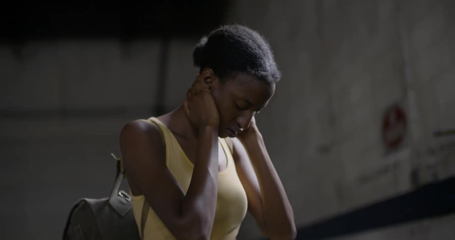 A woman holds her neck in a dark room