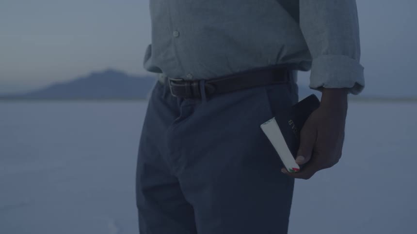 A man carrying a book walking on salt flats at sunset