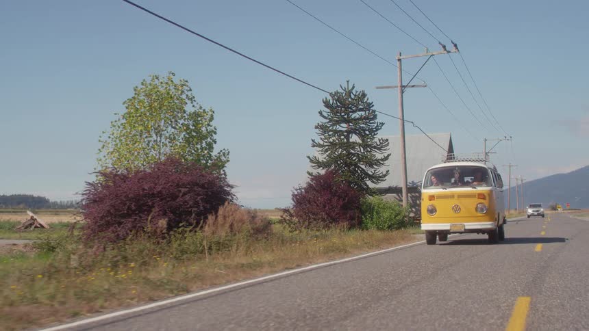 A vw van is being driven on a rural road on a sunny day