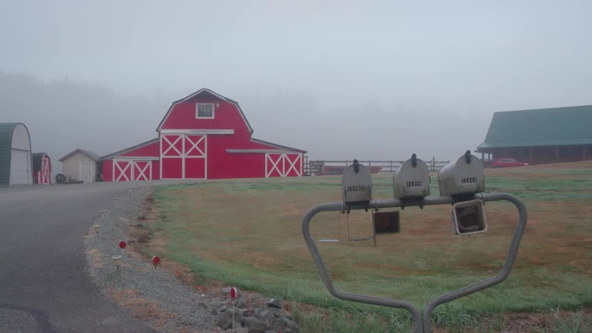 Clouds and fog are hanging over a farm and barn during the day