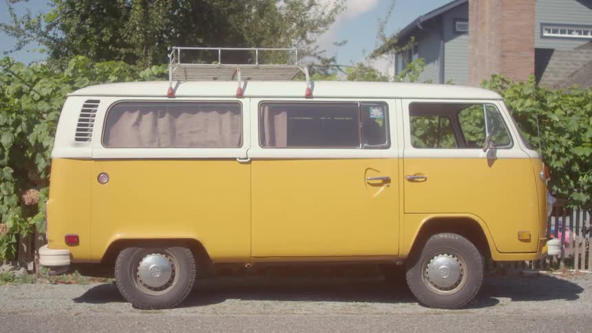 A yellow van sits parked next to vine covered fence