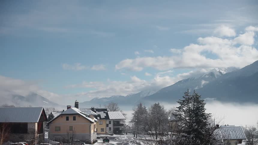 Clouds and fog passing above and through a small town in the mountains on a winter day