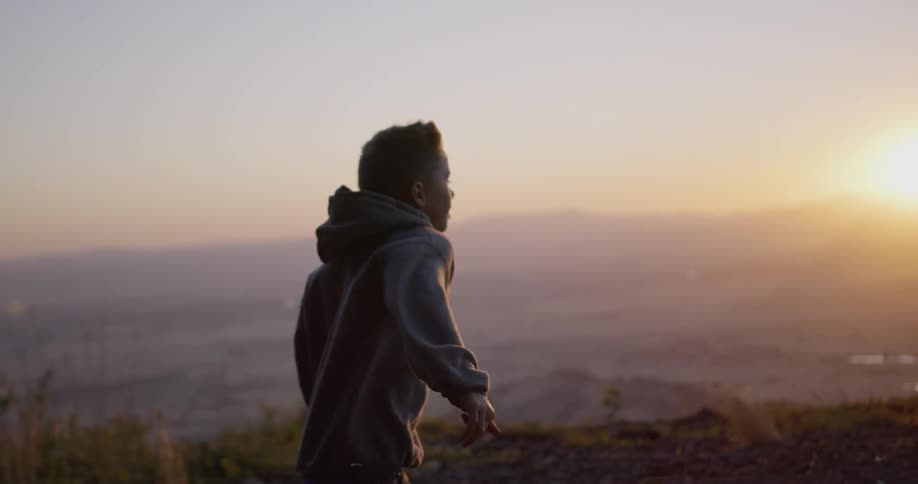 A boy and girl run along a ridge at sunset