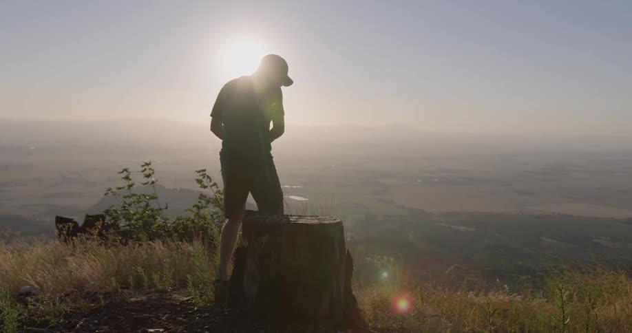 Man sits on a tree stump overlooking a valley at sunset