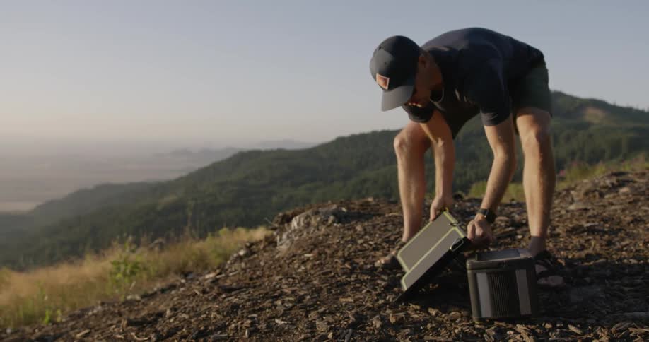 Man sets up solar equipment in mountains at sunset