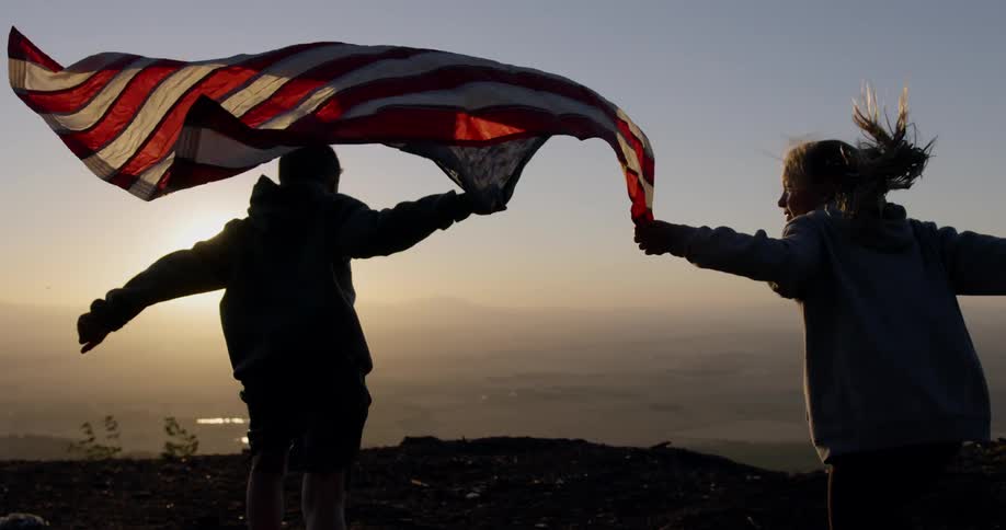 Two people run with an american flag at sunset