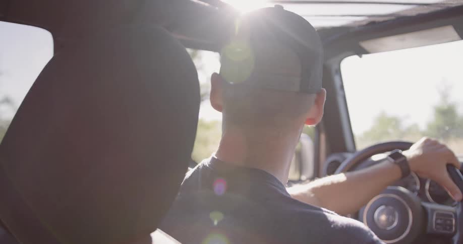 A man leans out the window of Jeep Wrangler while driving on a sunny day