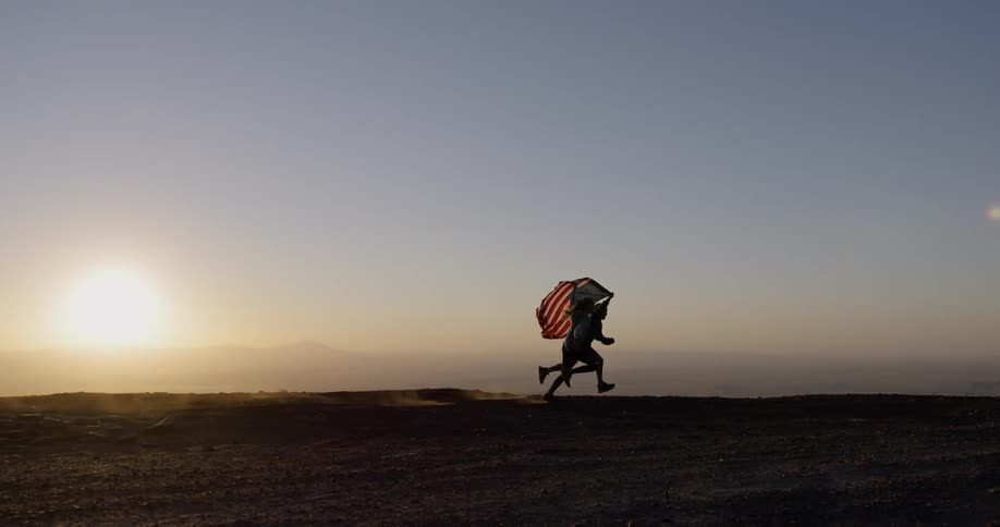 Children run while carrying a flag overhead at sunset