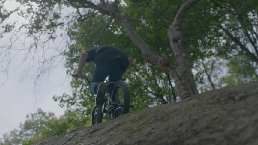 A boy rides a bike along a ridge near trees