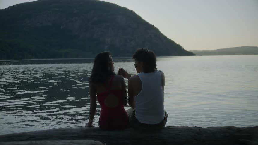 A man and woman smoking near a lake