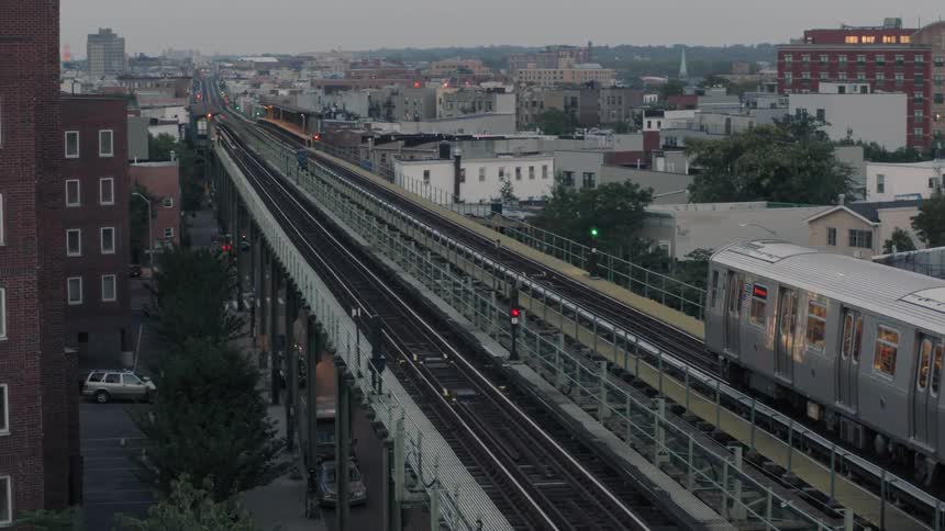 A commuter train is running on tracks above a city street at dusk