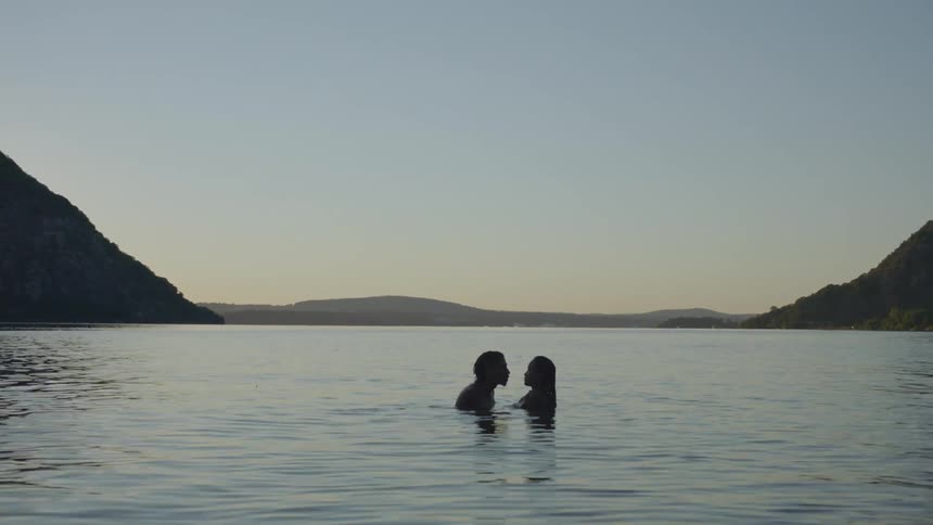 A man and woman kiss while swimming in a mountain lake at sunset