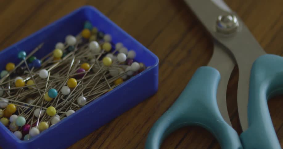 A pair of scissors sits next to pins