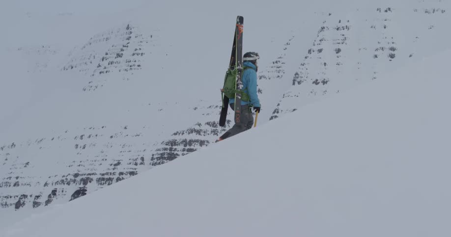 A skier hikes up a snowy mountainside