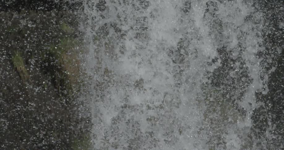 Water is crashing over a ledge and onto rocks below in a natural setting
