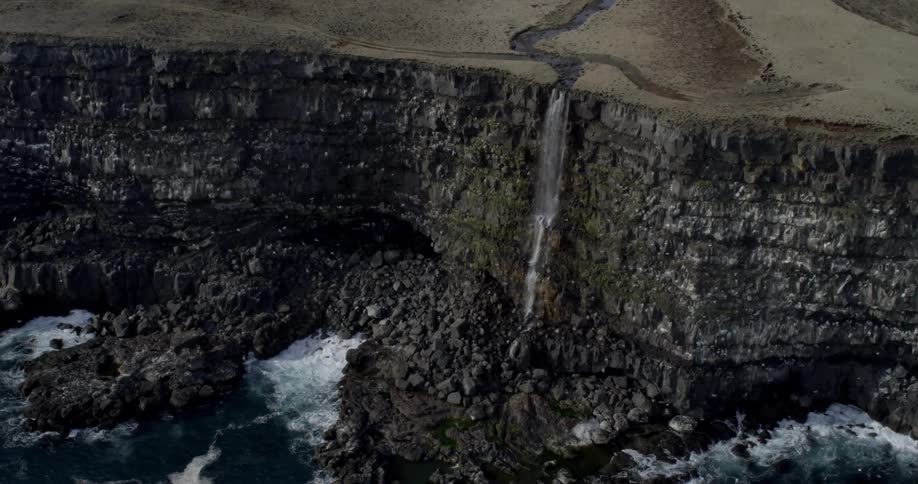 A waterfall cascades over a coastal cliff