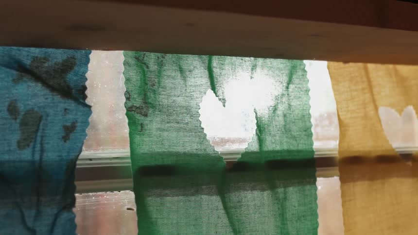 The sun is shining through fabric squares hung in a window