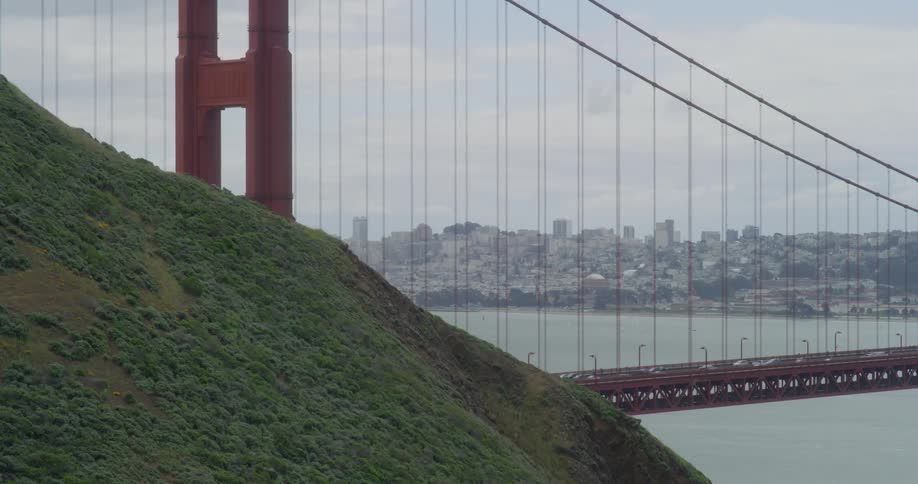 Cars drive over the golden gate bridge with city behind