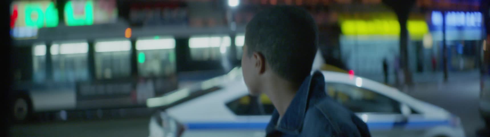 A teenage boy is walking on a city sidewalk at night