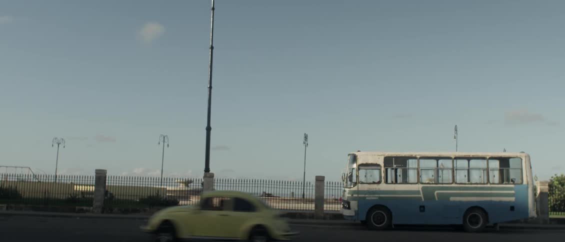 A bus sitting on a road with other traffic passing by in front of a large body of water