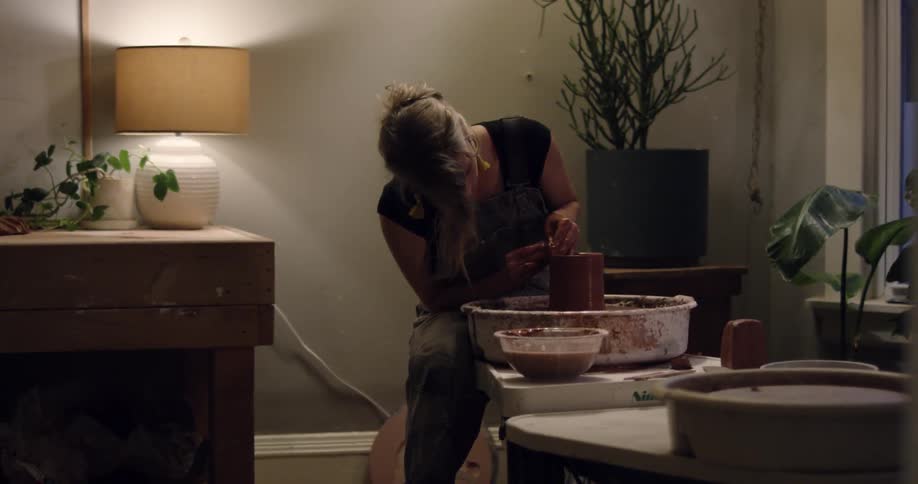 A woman making pottery inside her home at the table