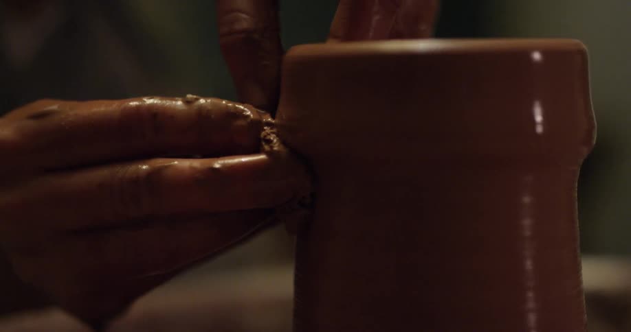 A woman is forming a piece of clay on a pottery wheel