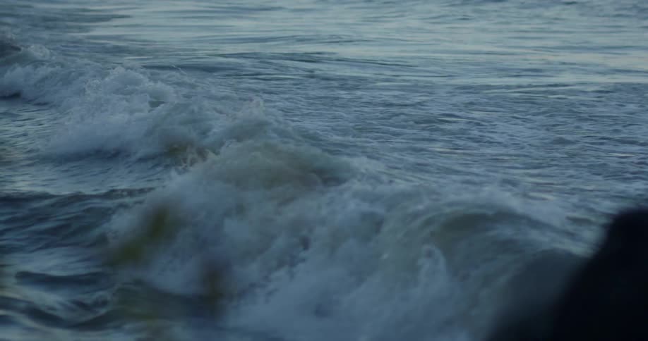 A wave is cresting and rolling toward the shore beyond a group of surfers