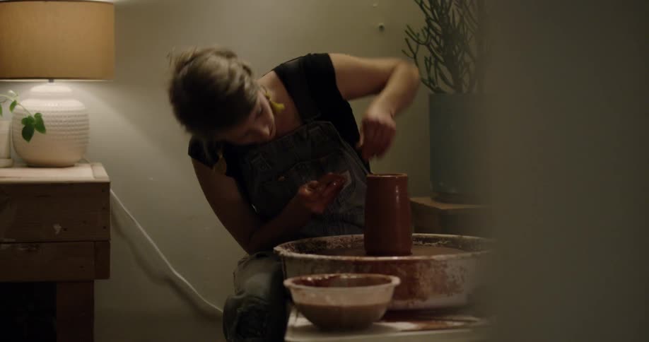 A woman making pottery inside her home at the table