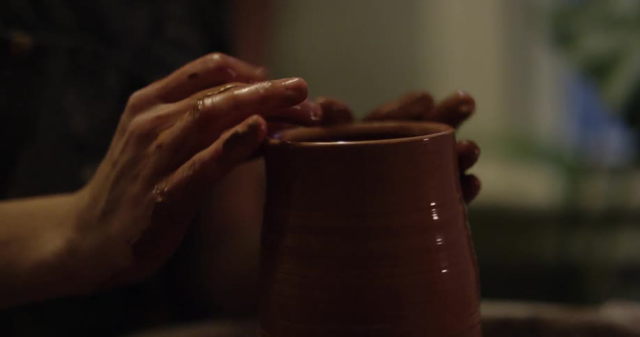 An artisan is forming clay into pottery on a wheel