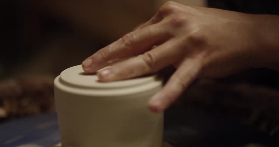 An artisan is forming clay into pottery on a wheel