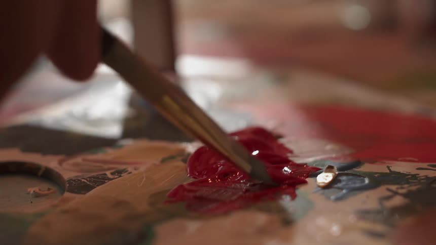 A person dips a brush in paint