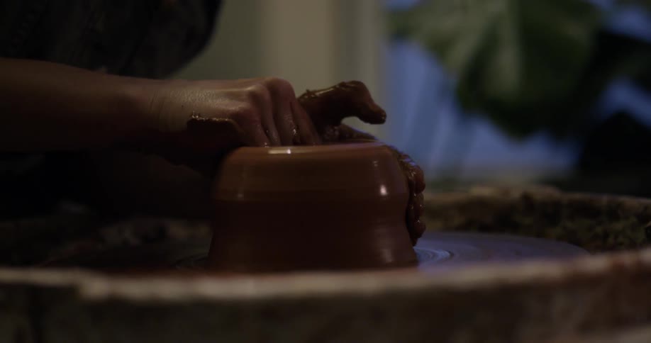A woman is forming a piece of clay on a pottery wheel