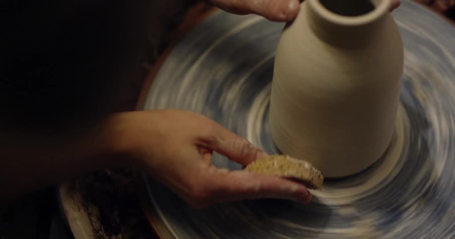 A person is using a sponge while forming a pottery vase