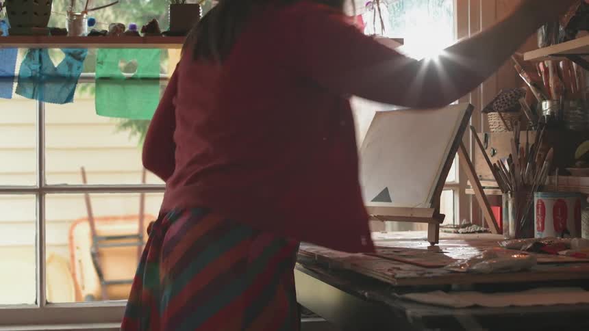 A woman places a canvas on an easel that is setting on a table