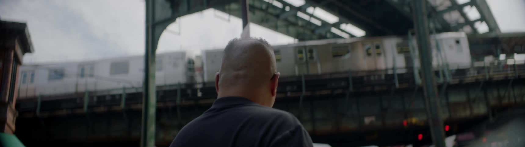 Man walks through a city as a train passes overhead
