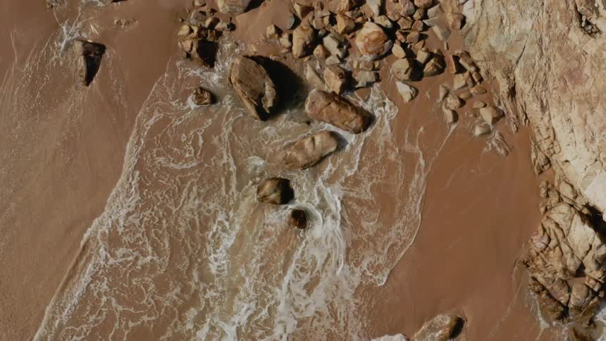Waves rolling onto a sandy beach littered with rocks