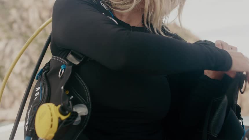 A woman is putting on a diving vest on a boat outside during the day