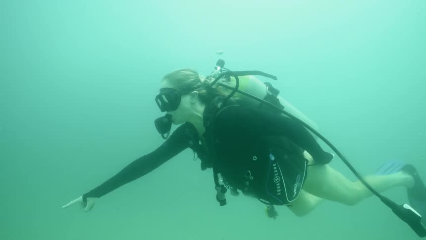 A female diver is swimming and pointing to something underwater during the day