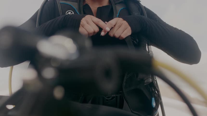 A woman wearing a scuba suit snaps her equipment vest on