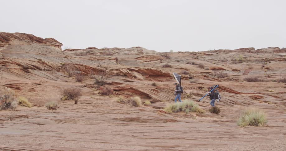 A camera crew totes equipment across a rocky terrain
