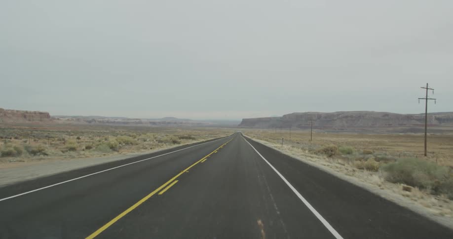 A vehicle drives down a rural road surrounded by empty fields
