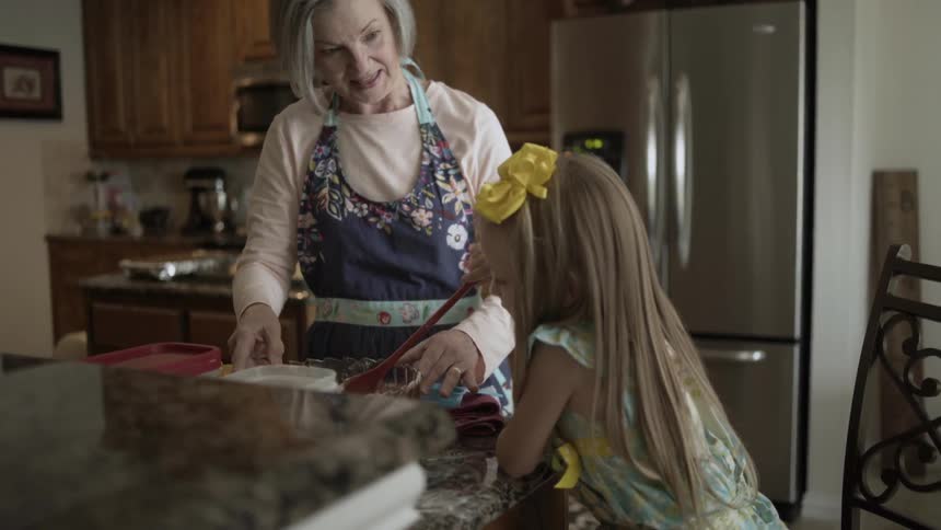 A girl helps her grandmother stir the batter in the kitchen