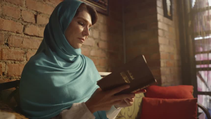 A muslim woman is reading from a book inside during the day