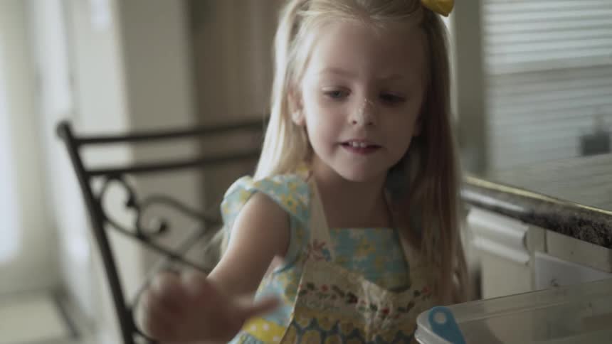 A girl scoops up flour in a measuring cup and adds it to the bowl